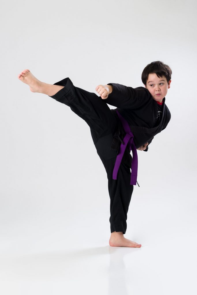 Youth karate student in a black gi throwing a high side-kick at Arashi-Do Red Deer