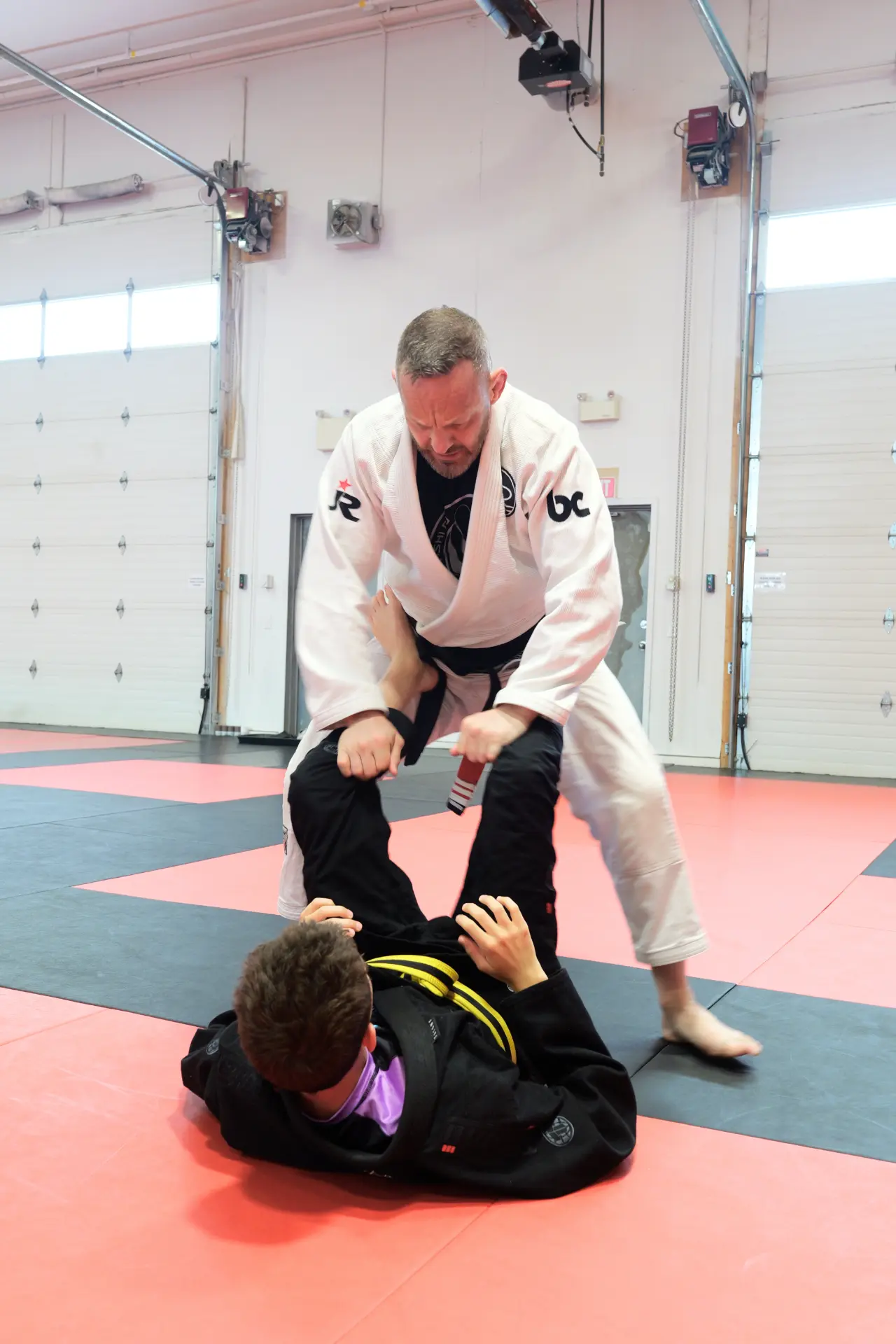 Instructor controlling a student's legs while passing guard during a Brazilian Jiu Jitsu drill