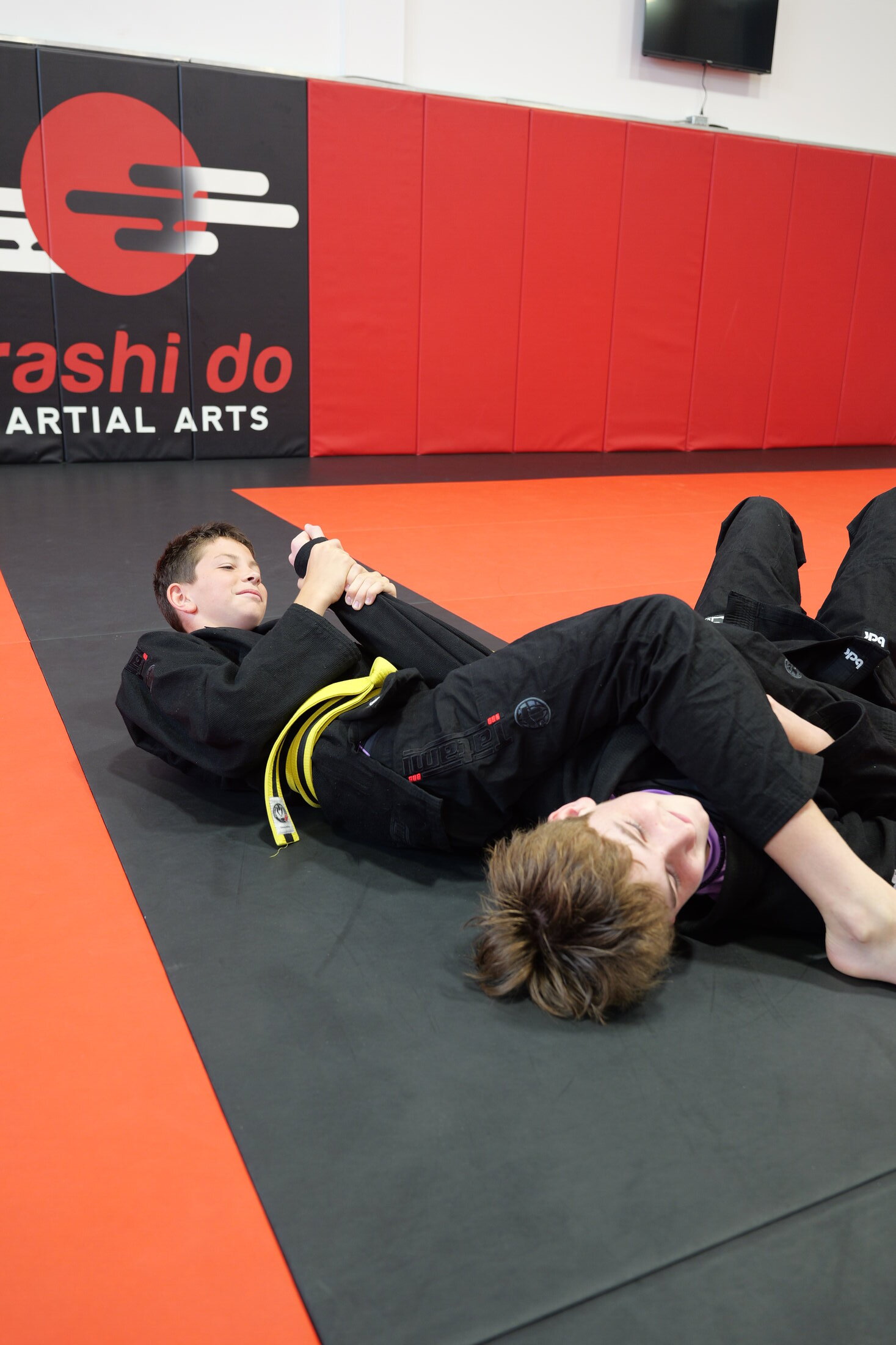 Two students grappling on the mat, one finishing an armbar from the bottom during ground-fighting practice